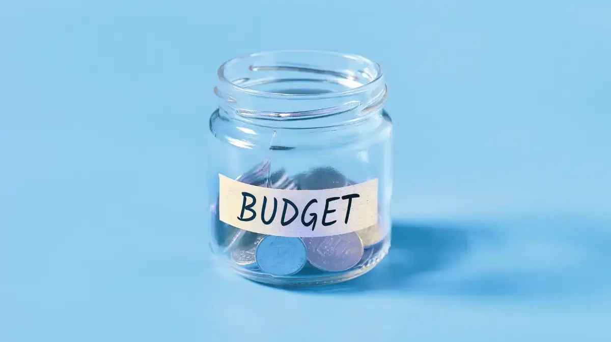 glass jar that has budget taped across it on a tabletop with a blue background