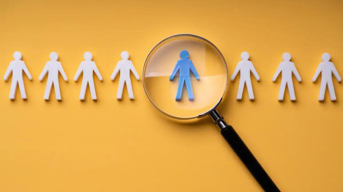 yellow background with cutouts of people in white and a blue person inside of a magnifying glass