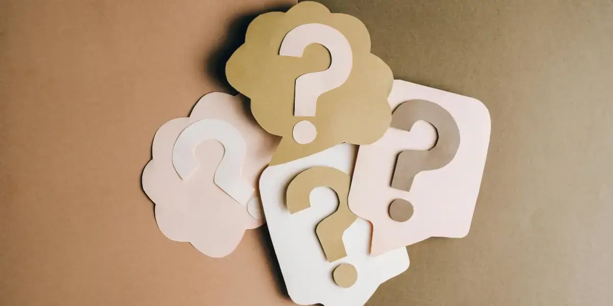 Paper cutouts with question marks arranged on a neutral background.