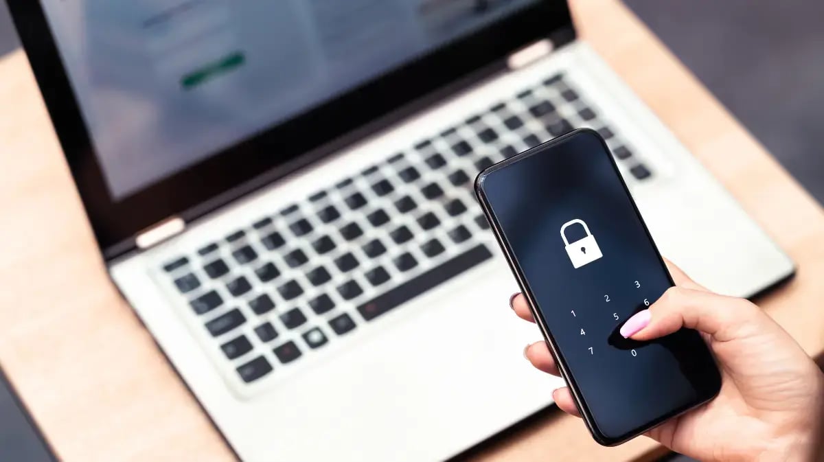laptop open with a person holding a phone in the hand with a lock on the screen