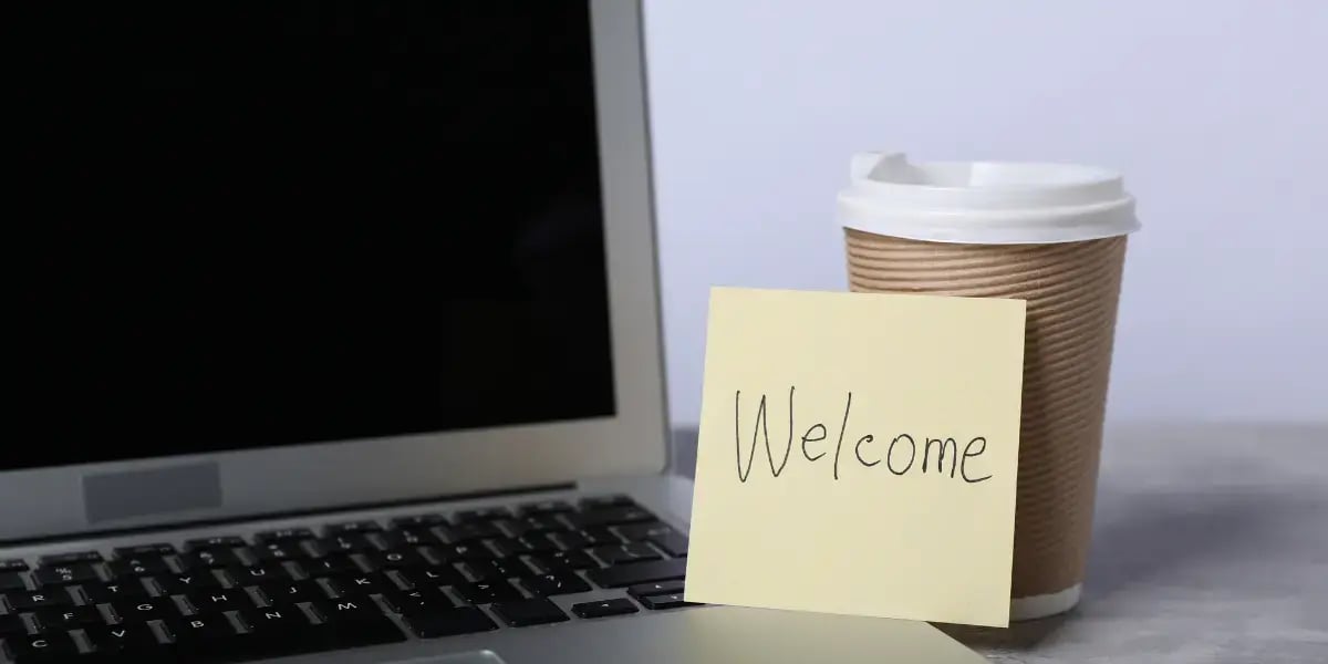 coffee cup and laptop on a desk with a sticky note that reads 