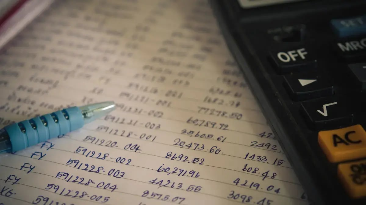 paper with written numbers and transactions on it with a calculator and pen on top